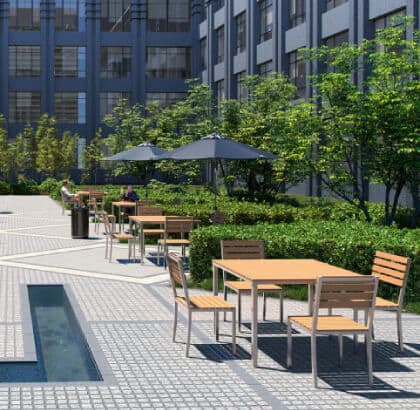 Modern outdoor dining area with wood and metal tables and chairs, surrounded by greenery and shaded by umbrellas